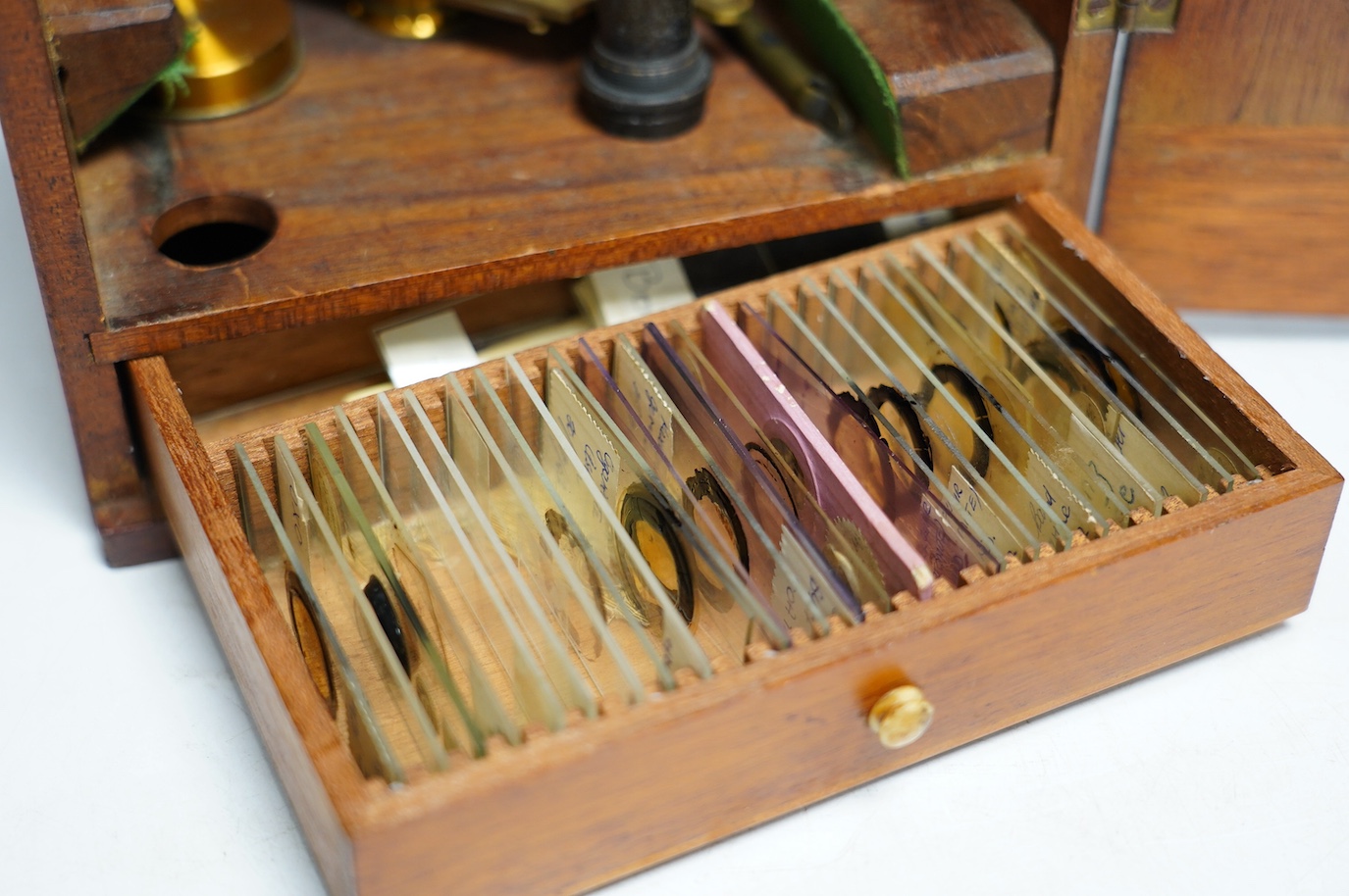 An unmarked late 19th century monocular brass microscope, in a fitted mahogany case with alternative lenses, a drawer for slides and other accessories, case 39cm high. Condition - fair to good